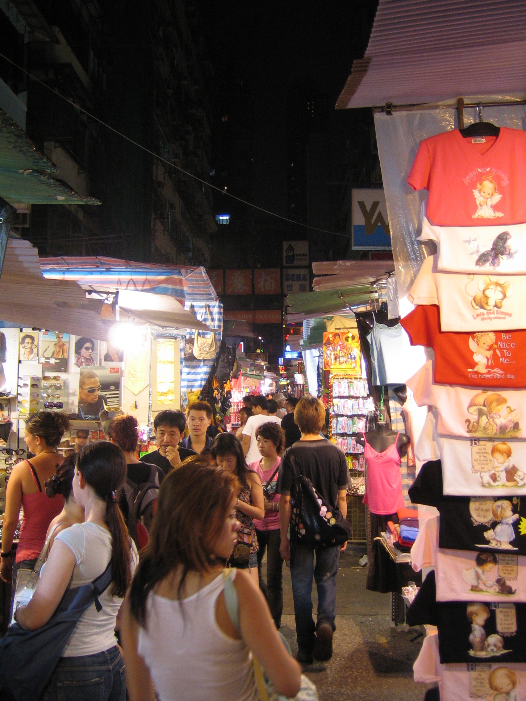 Bustling Temple Street Night Market stalls with hanging clothes and shoppers navigating the crowded street at night